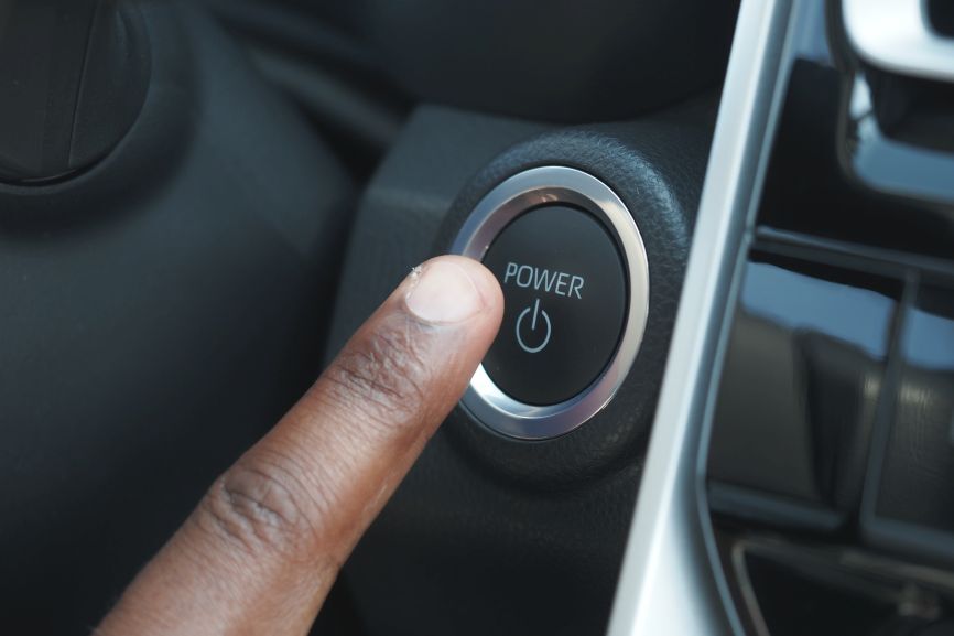 Driver pressing the engine start button inside a modern car, highlighting a common situation where a car loses power when accelerating due to overlooked engine or electrical issues.
